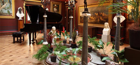 Museum hallway with piano paintings and plants shown